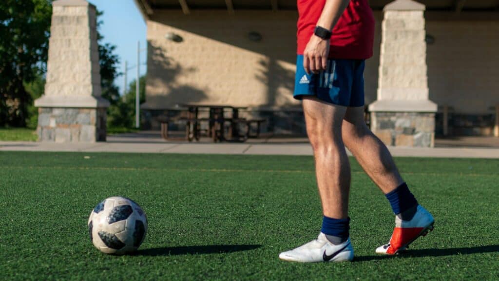 man in red shirt and blue shorts playing soccer during daytime