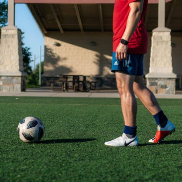 man in red shirt and blue shorts playing soccer during daytime