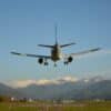 Commercial airplane landing with snow-capped mountains under a blue sky