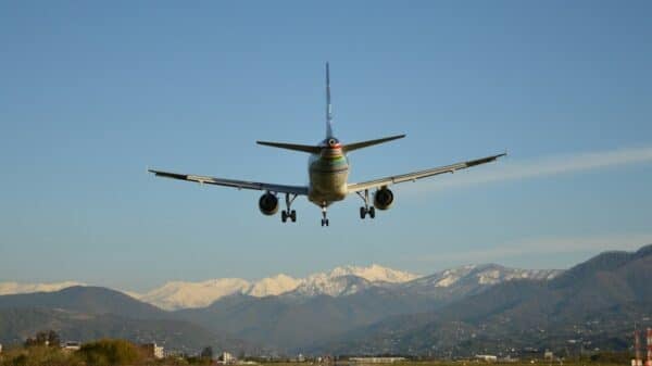 Commercial airplane landing with snow-capped mountains under a blue sky