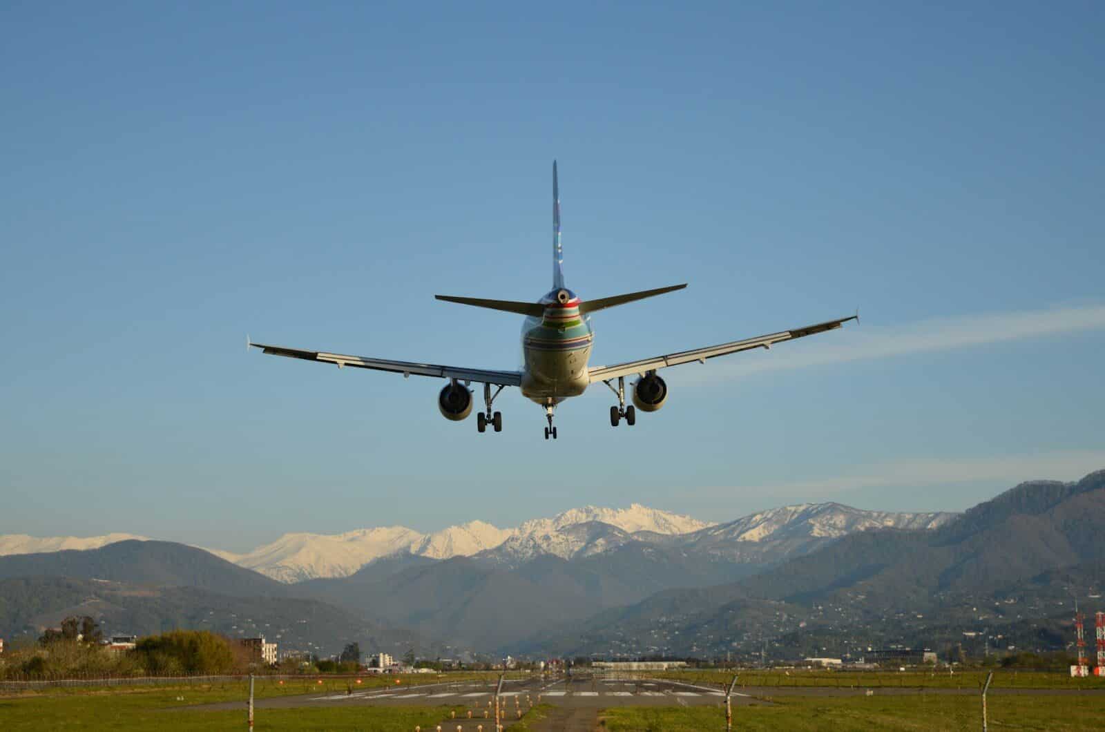 Commercial airplane landing with snow-capped mountains under a blue sky