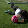 woman in white long sleeve shirt and black pants playing soccer on green grass field during