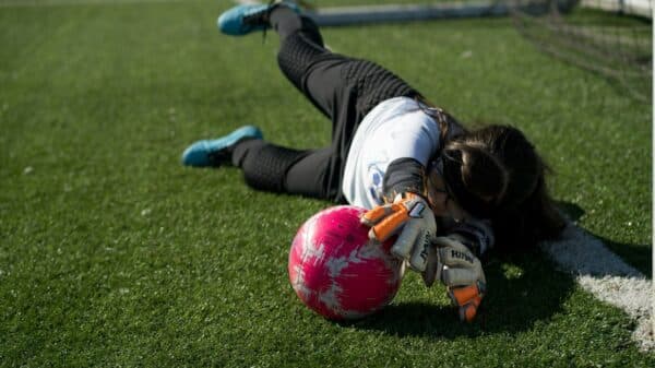 woman in white long sleeve shirt and black pants playing soccer on green grass field during